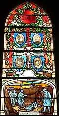 Photographie en couleurs d'un vitrail représentant des portraits surmontant une scène de guerre.