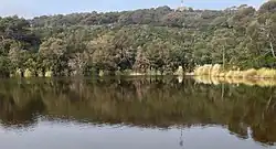 Photographie couleur. Les collines entourant cette modeste étendue d'eau sont couvertes d'arbres de faible hauteur et de la garigue.