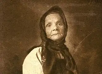 Photographie sépia d'une vieille femme portant un fichu sombre.