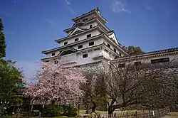Château de pierre blanche de style oriental. Des cerisiers en fleurs sont également visibles.