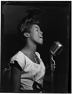 Une femme noire-américaine de profil, en robe claire, en train de chanter les yeux fermés