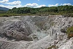 Photographie d'une crevasse rocheuse avec un peu de liquide au fond. Une fumée fine s'échappe du trou.
