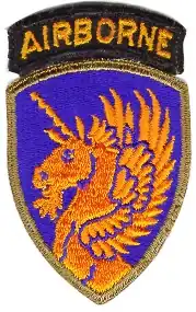 Écusson représentant une licorne ailée orange doré sur fond bleu surgissant du bas de l'écusson