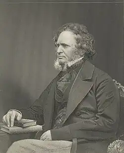 Gravure d'un homme aux cheveux mi-longs bouclés avec des favoris portant un costume et assis la main sur un livre