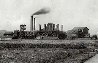 Anciens bâtiments industriels en bois, pierre et brique surmontés de multiples cheminées.