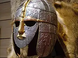 Photo d'un casque couvrant visage et oreilles aux motifs ciselés représentant des scènes de guerre