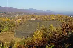 Deux terrils semi-coniques, l'un de teinte rouge et l'autre noir sont en partie couvert d'arbres dans une plaine.