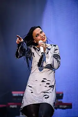 Image d'une femme brune chantant dans un micro et portant une robe blanche et noire