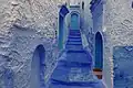 Une impasse, formée d'un escalier en légère pente, finie par une porte, avec des maisons bleues.