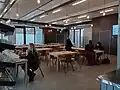 Tables et bancs sont disposés dans un grand local lumineux.