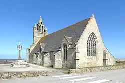 À gauche, le calvaire. Au fond, le clocher-mur avec ses deux tourelles. La façade sud, avec grands contreforts, est percée de deux baies. Au premier plan, le chevet, percé d'une grande baie, est prolongé par le pignon de la remise.