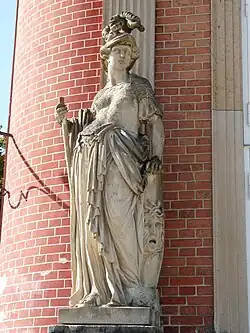Statue d'une femme en armure. Elle porte un casque, un bouclier et une lance.
