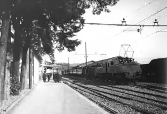 Photographie en noir et blanc d'une grande locomotive électrique tractant une rame sous une caténaire.