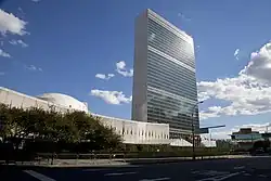 Un haut bâtiment est visible, de nombreux drapeaux au premier plan.
