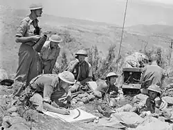 Sept hommes en treillis militaire utilisant des radios et des mégaphones.