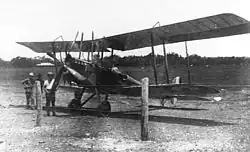 Photo en noir et blanc d'un biplan sur un air d'atterrissage avec deux hommes à côté.