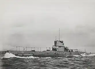 Photographie d'un sous-marin en surface. Plusieurs marins se trouvent sur le pont du submersible.