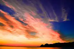 Le soleil couchant avec beaucoup de nuages rouges et une montagne.