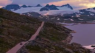 Voiture sur une route le long d'un lac avec un vaste glacier en arrière-plan.