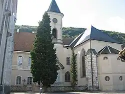 Photogaphie couleur du clocher et du chevet d'une église, dominant un petit cimetière planté d'arbres.