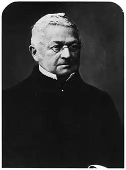 Photographie en noir et blanc d'Adolphe Thiers, haut du corps seulement. Il arbore un habit entièrement noir qui fait ressortir ses cheveux blancs et son visage. Il porte ses petites lunettes ovales.