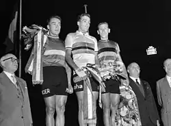 Photographie en noir et blanc montrant trois cyclistes sur un podium entourés par deux officiels.