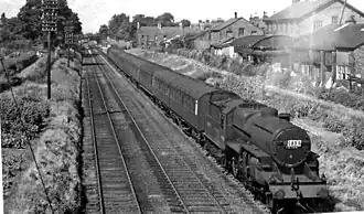 Photo noir et blanc, voie ferrée, train à vapeur, maisons sur les berges.