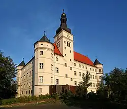 Photo en couleurs (18 août 2005) du château de Hartheim, en Bavière, centre d'euthanasie ouvert pendant la période nazie. La couleur beige très clair des deux façades visibles du château, à l'architecture de type Renaissance, contraste contre le ciel bleu, en arrière-plan, et la verdure au premier plan.