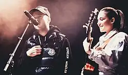 Photographie de la même chanteuse accompagnée d'un jeune homme en concert.