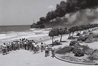 Cargo avec un incendie partant du centre du pont, très proche de la plage, dégageant une fumée très épaisse.