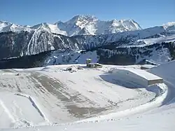 Photographie en couleurs d'une vue prise en hauteur vers l'altiport avec les montagnes dans le fond.