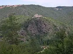 photo couleur d'un hameau avec un clocher au sommet d'une crête rocheuse cernée de pentes abruptes couvertes de forêt.