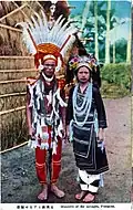 Carte postale : une photo montre un couple habillé en costume traditionnel devant une hutte.