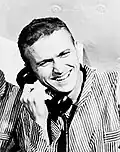 Photographie en noir et blanc de Borman souriant au téléphone.