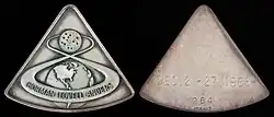 Deux médailles de forme triangulaires, sur celle de gauche le trajet Terre-Lune d'Apollo.