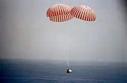 Un vaisseau spatial descend au-dessus de l'océan avec des parachutes.