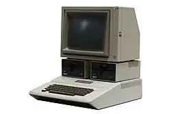 Ordinateur gris équipé d'un clavier, de deux lecteurs de disquette et d'un petit moniteur.