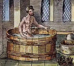 Homme s'immergeant dans une baignoire en bois installée dans une pièce.