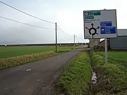 La route départementale 273 arrivant sur le giratoire de l'autoroute et un panneau diagrammatique à droite