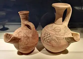 Deux vases à bec verseur peint de motifs linéaires et sinueux rouge sur fond clair.