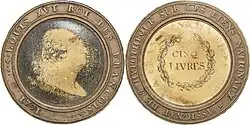 Pièce de monnaie avec gravure sur carton au centre, insérée dans une couronne en métal de cloche.