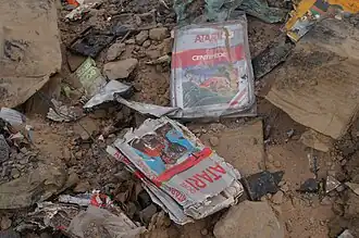 Amoncellement de détritus et de gravas, dont parmi ceux-ci figure une cartouche des jeux vidéo E.T. et Centipede très détériorées (de couleur grise, rouge et bleue).