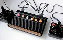 Boite noire avec deux manettes de jeux noires, comportant quelques pointes de marron et des boutons jaunes.