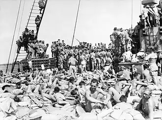 Photo en noir et blanc d'une cinquantaine d'hommes rassemblés sur le pont d'un navire. Ceux qui sont au premier plan sont en train de se bronzer. Ceux qui sont à l'arrière-plan tournent le dos à l'objectif.