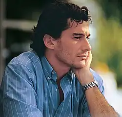 Photographie en couleur d'un homme blanc, brun, vu de profil droit, en plan poitrine, tenant sa tête dans sa main gauche, avec une chemise bleue.