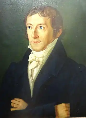 Portrait sur fond vert d'un homme en buste tourné vers la droite, cheveux bruns courts, les bras croisés, collet monté et portant une veste sombre.