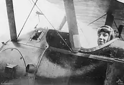 Photographie en gros plan du flanc d'un avion. Un homme portant une casquette et des lunettes de protection sur le front est assis dans le cockpit.