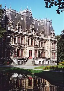 Vue d'un bâtiment de trois étages avec de grands toits. Plan d'eau au premier plan dans l'ombre.