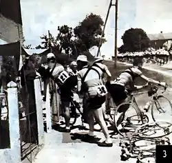 Photo en noir et blanc de trois cyclistes professionnels rentrant dans un café pour se ravitailler.