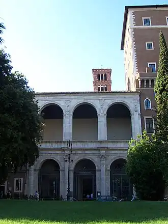 Image photographique d'une façade d'édifice composée trois arches sur piliers sur deux ordres.